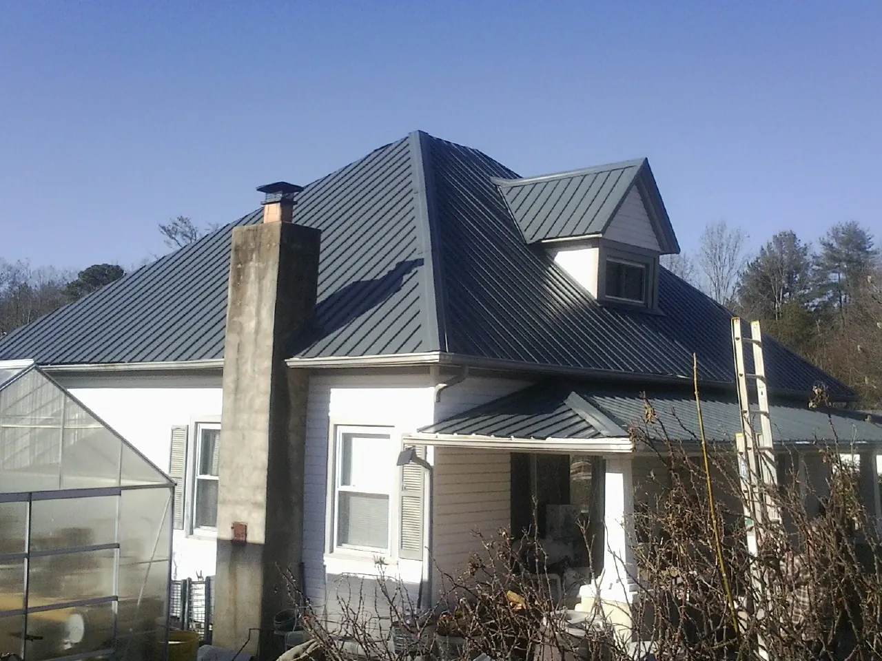 Dark blue standing seam metal roof on a white farmhouse with dormer — Slate & Tile Roof Repair by Roofing Brothers in Ewell