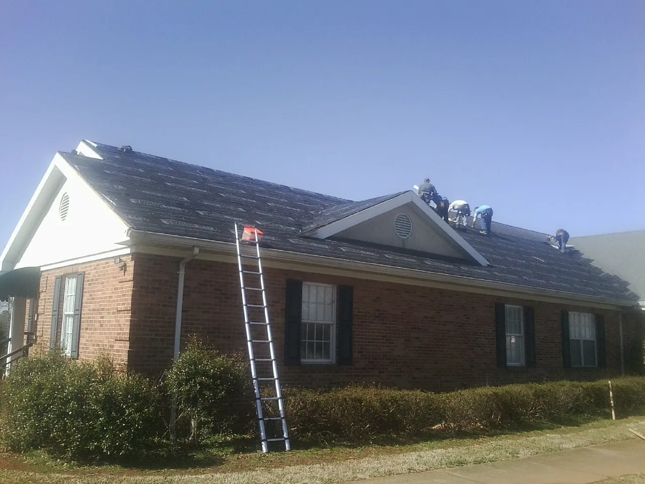 Crew tearing shingles off a brick ranch roof with a ladder set — Emergency Roof Repair work by our crew in Ewell