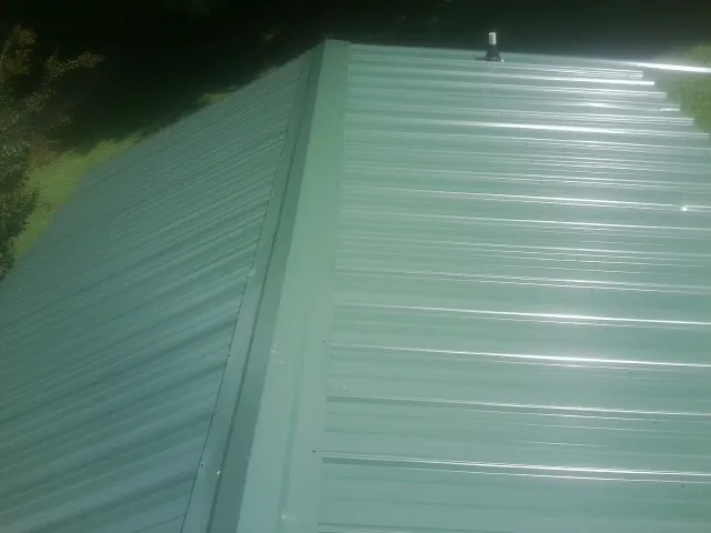 New green metal panels meeting at the ridge of a roof — Flat Roof Repair work by our crew in Ewell